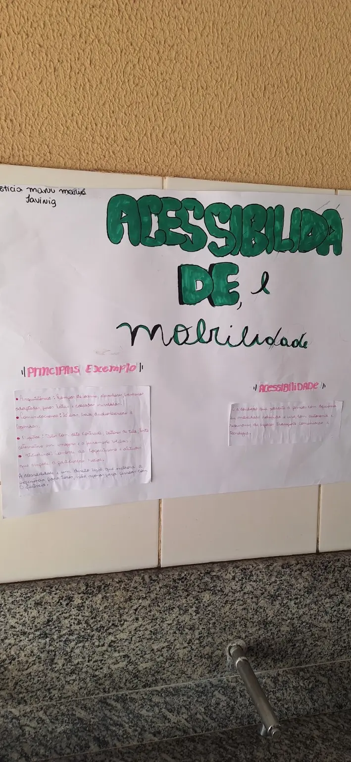 Fotografia vertical de um cartaz branco feito à mão. O título Acessibilidade e mobilidade aparece em letras grandes verdes. A parte inferior contém pequenos quadros de texto sobre princípios, exemplos e o direito à mobilidade.