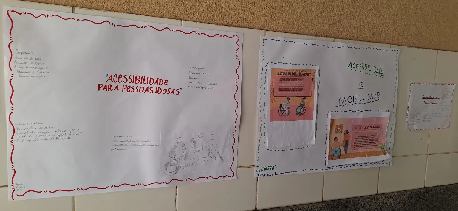 Fotografia panorâmica de cartazes afixados em uma parede. O maior, contornado em vermelho, traz o título Acessibilidade para pessoas idosas e anotações sobre arquitetura, comunicação e tecnologia. Ao lado, outro cartaz reúne textos e ilustrações sobre acessibilidade e mobilidade.